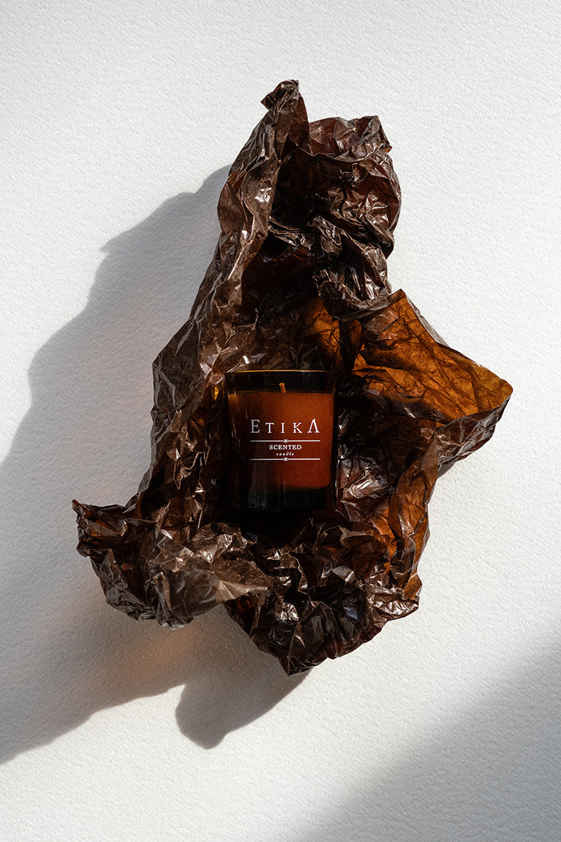 Candle labeled 'Etika' wrapped in crumpled brown paper on a white background